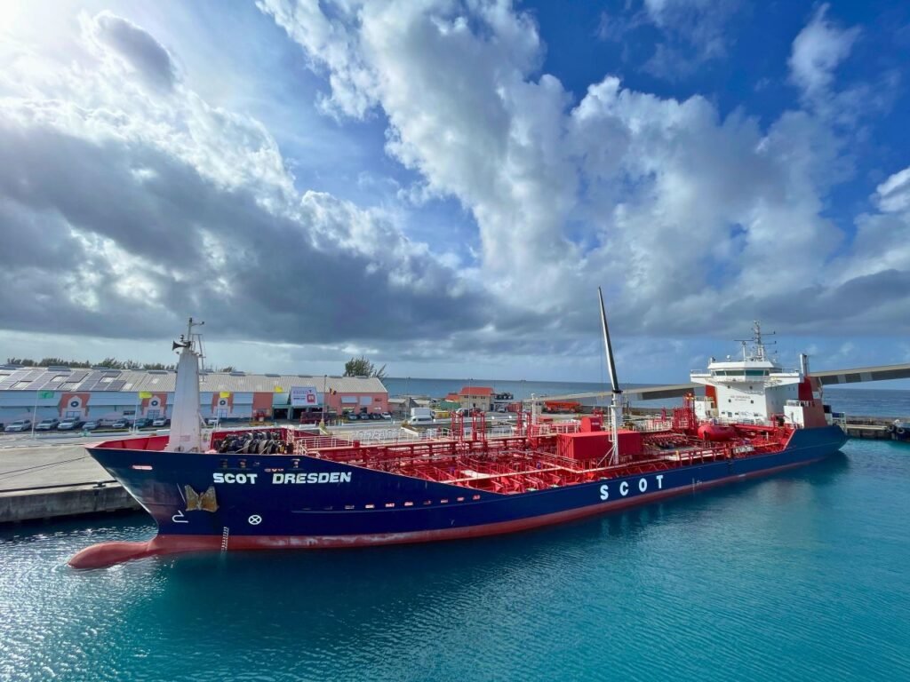 a large container ship docked at a vibrant harbor in barbados under a partly cloudy sky