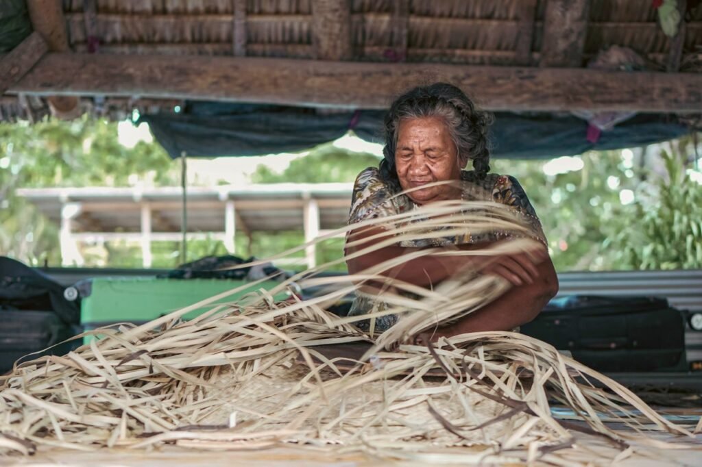 an elderly woman skillfully weaves a basket using natural materials in an outdoor setting in kiribati.