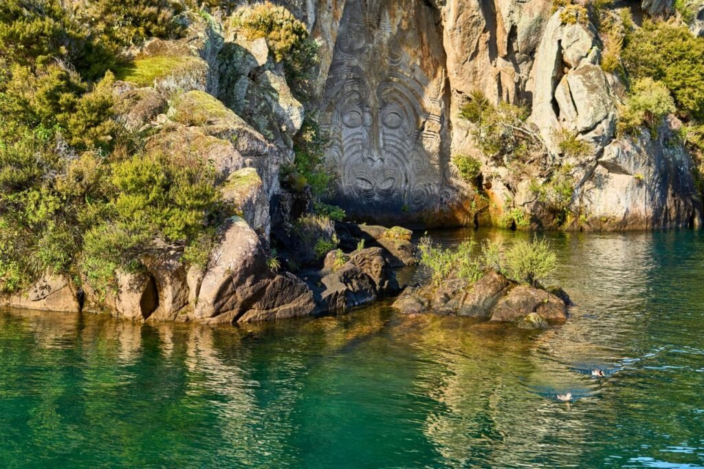 serene landscape of maori rock carvings at mine bay, lake taupō with clear waters and lush greenery taupō, waikato region, new zealand