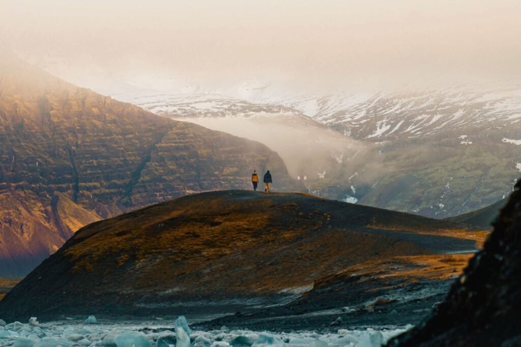 two hikers traverse a scenic, snow capped mountain landscape in iceland.