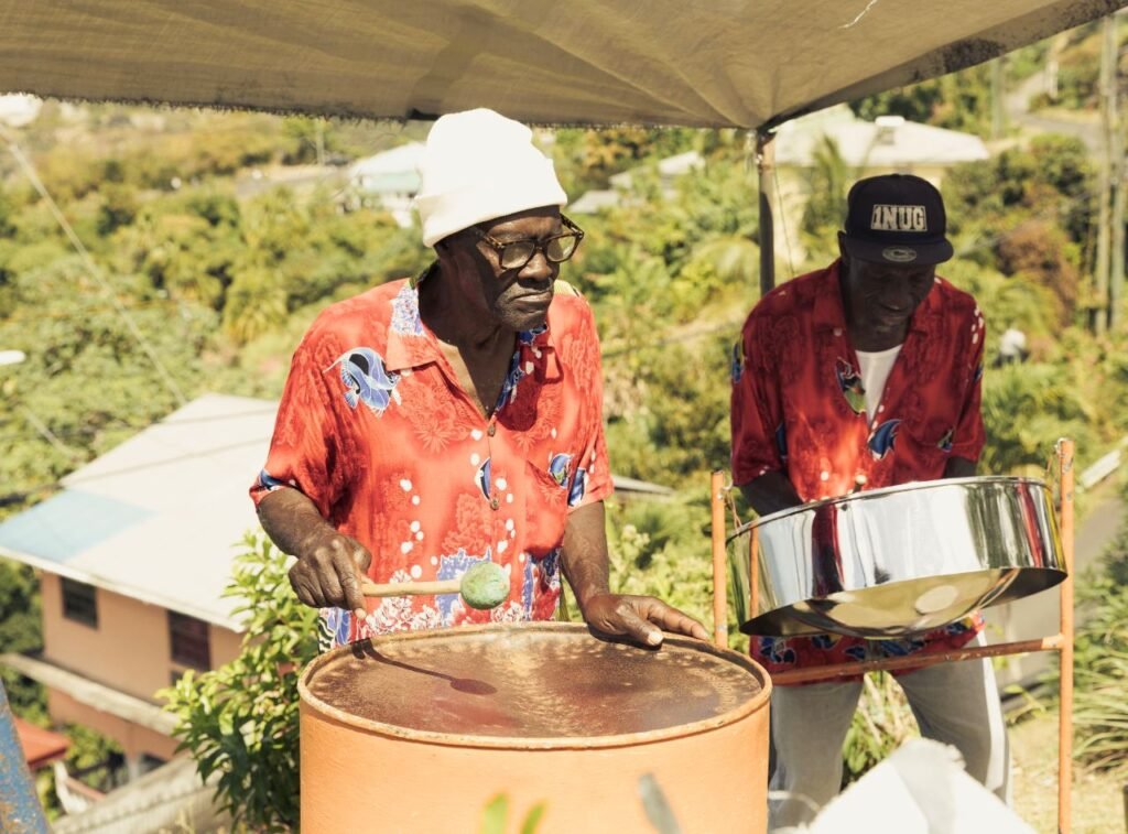 two musicians play steel drums in a tropical outdoor setting with vibrant shirts and hats trinidad and tobago