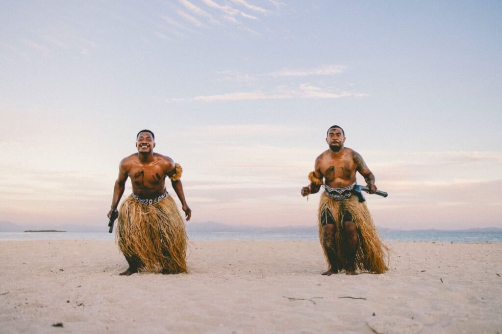 two traditional fijian warriors perform on a sandy beach in nadi, fiji, at sunset